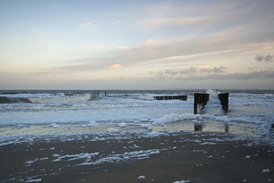 Rear view of man standing at beach against sky during sunset