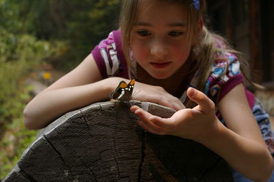 Girl looking at butterfly on tree stump