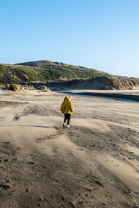 Boy walks on sandy beach tword fresh water stream leading to ocean