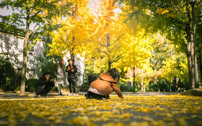 Rear view of girl playing with fallen autumn leaves in park