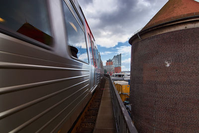 Train on railroad track against cloudy sky in city
