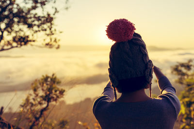 Rear view of young woman standing against sky during sunset