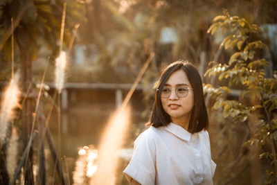 Portrait of beautiful young woman standing against plants