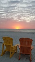 Chairs and tables at beach against sky during sunset