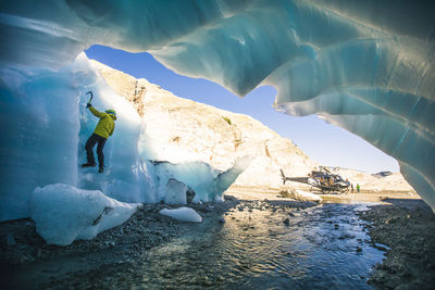 Ice climber climbing on glacial ice next to helicopter.