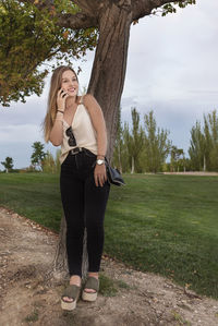 Full length portrait of woman standing on field against trees