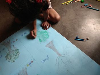 High angle view of girl drawing on paper while sitting on floor