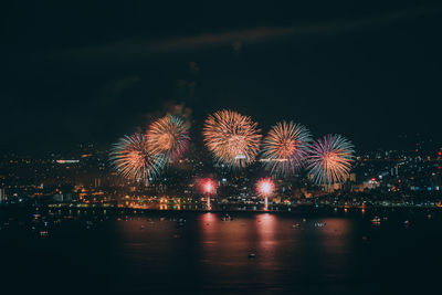 Firework display over illuminated city against sky at night