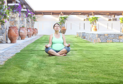 Full length of pregnant woman meditating on grassy land