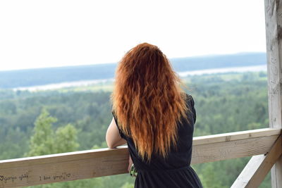 Rear view of woman leaning on railing against green landscape