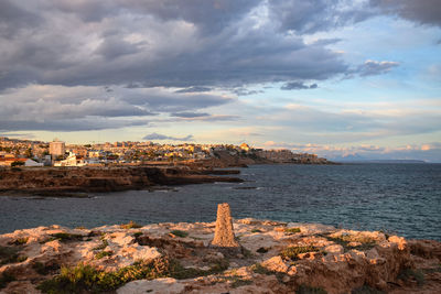 Buildings by sea against sky during sunset