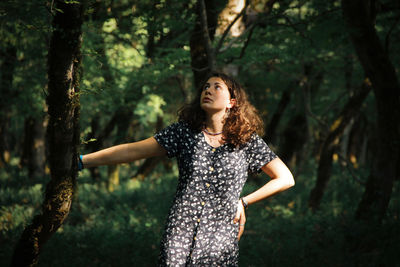 Young woman standing by tree trunk in forest