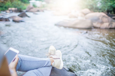 Low section of woman using mobile phone while sitting by river