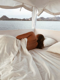 Shirtless woman lying on bed against sea