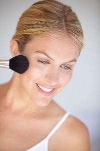 Close-up of young woman applying make-up against white background