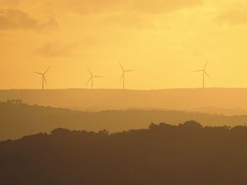 Wind turbines on field against sky during sunset