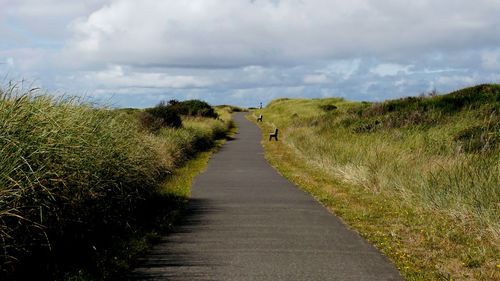 Empty road amidst grass against cloudy sky