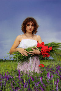 Young woman standing by purple flower on field against sky