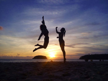 Silhouette female friends jumping at beach against sky during sunset