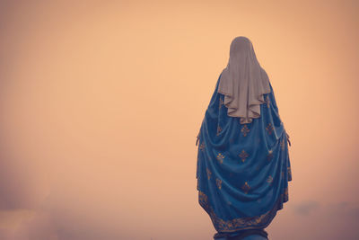 Rear view of woman standing against orange sky