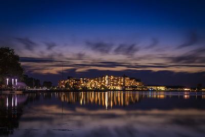 Illuminated buildings by lake against sky at night
