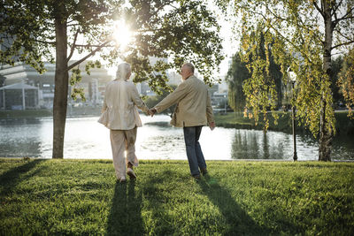 Couple holding hand while walking on grass by lake