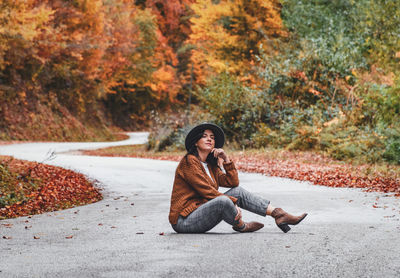 Young woman in autumn clothes sitting in the middle of road. fall colors, style.