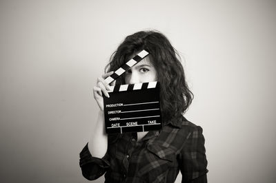 Portrait of young woman holding film slate against wall