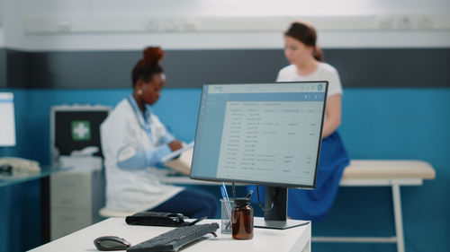 Close-up of computer with doctor and patient in background