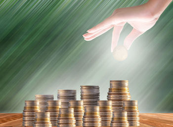 Digital composite image of hand holding coin over stack on table