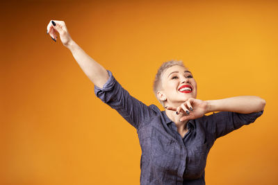 Happy woman with arm raised standing against orange background