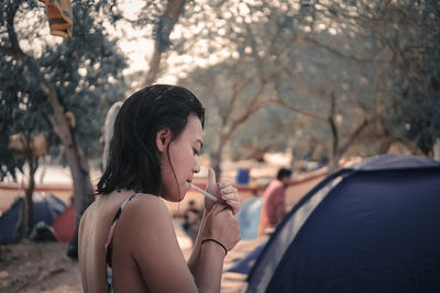 Close-up of woman lighting cigarette against trees