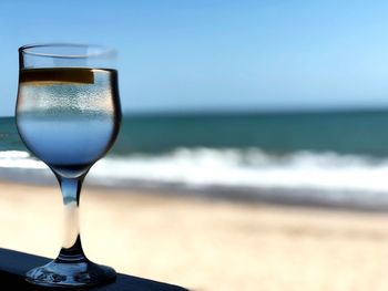 Close-up of beer glass on beach against sky