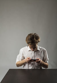 Rear view of boy using mobile phone while sitting on table