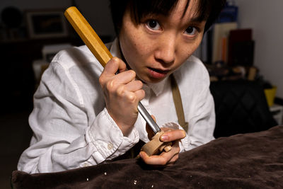 Young chinese female violin maker working with gouge to making a new violin in her workshop