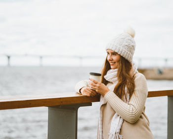 Young woman holding coffee while standing outdoors during winter