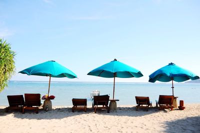 Beach umbrellas with lounge chairs on beach against sky