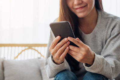 Midsection of woman using mobile phone while sitting on sofa at home