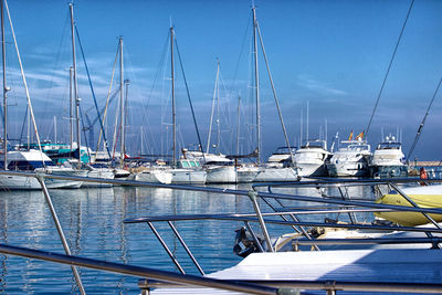 Sailboats moored at harbor against blue sky