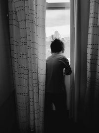 Rear view of man looking through window at home
