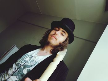 Low angle portrait of young man holding wooden post at home