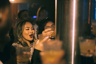 Happy young woman holding drink enjoying dance with friends at nightclub