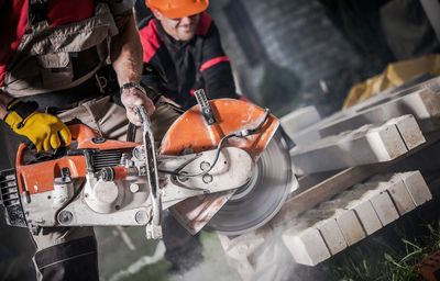 Midsection of worker using circular saw at construction site