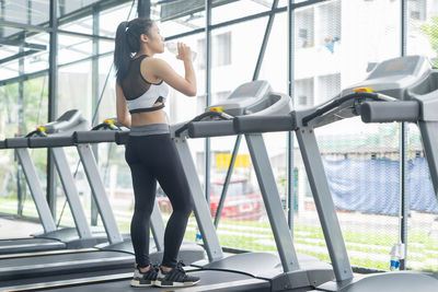 Young woman drinking water from bottle on treadmill at gym