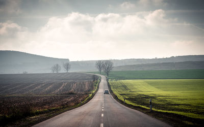 Empty road amidst field against sky