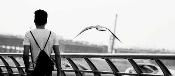 Rear view of man standing by railing against clear sky