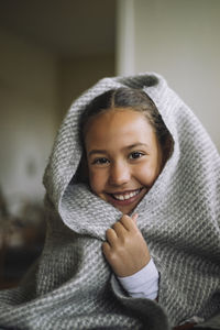 Portrait of smiling girl covered in blanket at home
