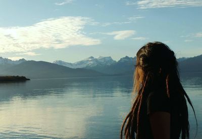 Rear view of woman standing by lake against sky