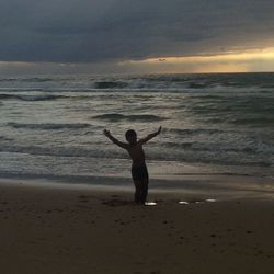 Full length of man on beach against dramatic sky