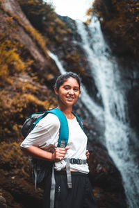 Portrait of young woman standing against waterfall